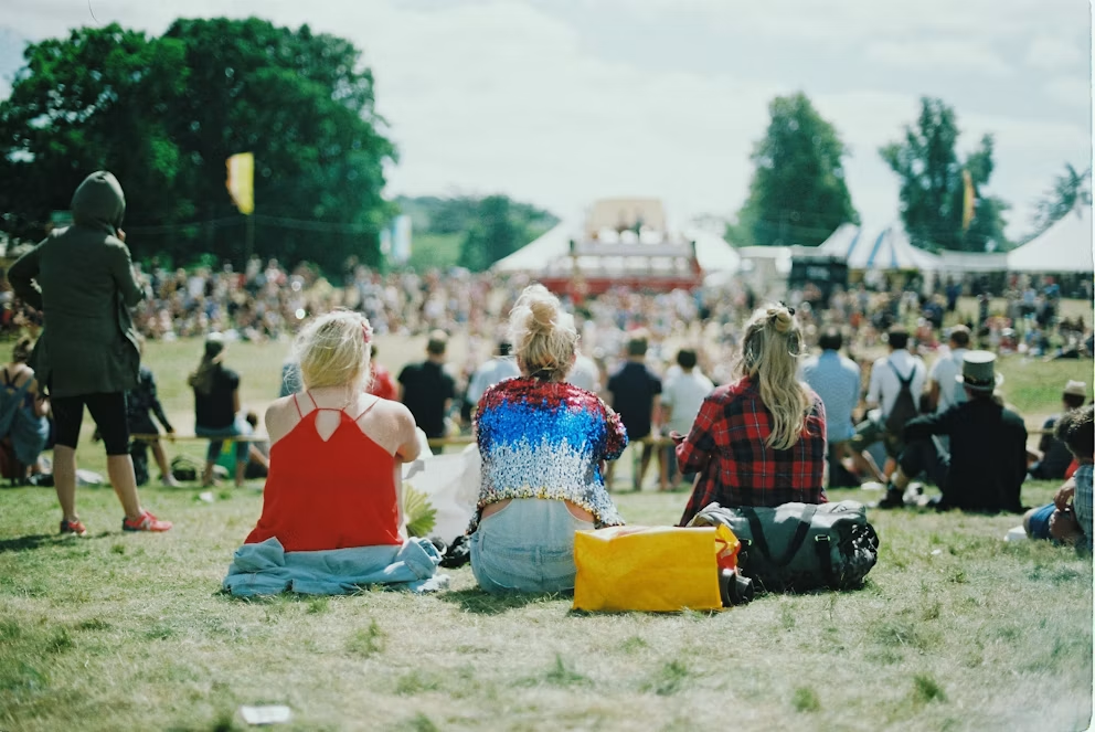 Festival-goers sitting on the grass watching a live stage on a sunny day