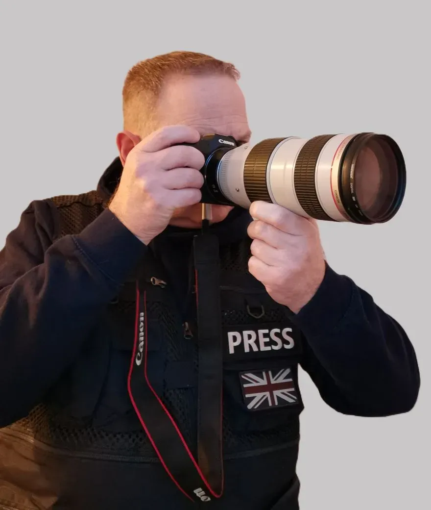 Lee, founder and lead photographer, shooting with a professional Canon camera and telephoto lens while wearing a PRESS vest